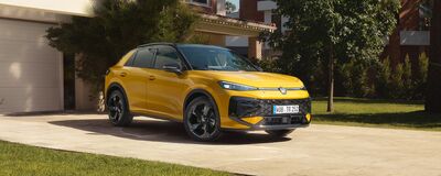 Ein gelber Volkswagen steht vor einem modernen Haus im Grünen, präsentiert von Volkswagen Zentrum Passau.