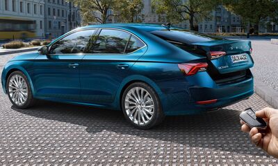 Blaue Škoda-Limousine auf gepflastertem Platz, mit einer Hand, die eine Fernbedienung hält. Škoda Auto Röhr.