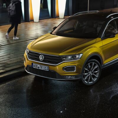 Ein goldener Volkswagen T-Roc parkt nachts auf nasser Straße, beleuchtet von Laternen nahe dem Volkswagen Zentrum Passau.