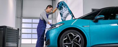 Eine Mechanikerin arbeitet an einem blauen Volkswagen in einer Werkstatt. | Auto Röhr.