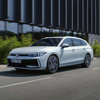 Ein weißer Volkswagen Passat fährt auf einer Straße, flankiert von modernen Gebäuden. Volkswagen Zentrum Passau.