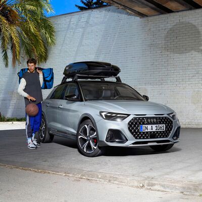 Mann mit Sporttasche und Basketball neben einem silbernen Audi mit Dachbox. Perfekt für den Urlaubs-Check. Audi Zentrum Passau.