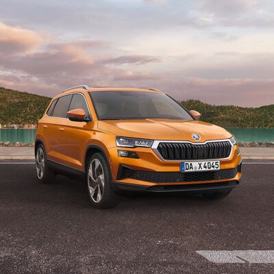 Orange Škoda Karoq SUV auf einer Straße vor einem See bei Sonnenuntergang. Škoda Auto Röhr.