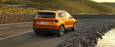 Ein orangefarbener Škoda Karoq fährt auf einer kurvigen Straße entlang eines Flusses. Škoda Auto Röhr.