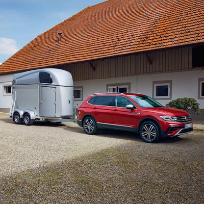 Ein roter Volkswagen mit Anhänger steht vor einem Gebäude, präsentiert von Auto Röhr.