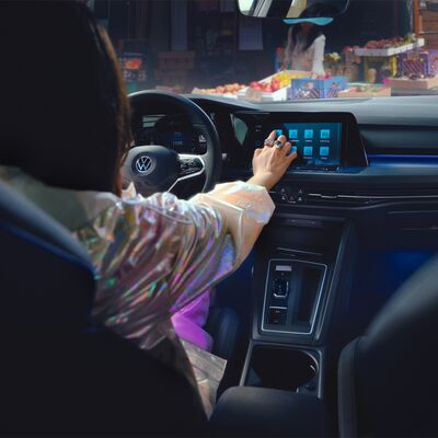 Frau bedient Touchscreen im Volkswagen Golf GTE, geparkt vor einem Marktstand. Škoda Auto Röhr.
