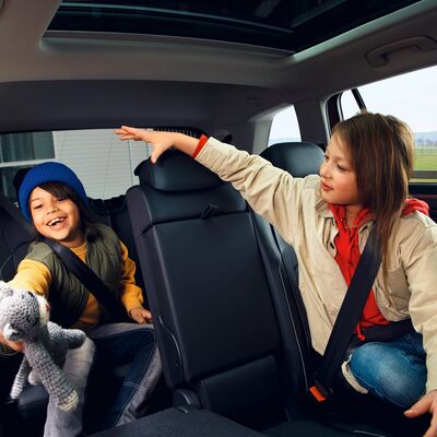 Zwei lachende Kinder spielen mit einem Stofftier auf der Rückbank eines Autos von Škoda Auto Röhr.
