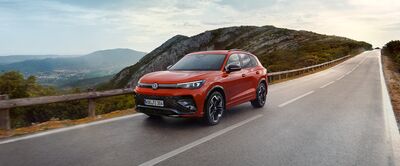 Ein roter Volkswagen fährt dynamisch auf einer malerischen Bergstraße, beworben von Auto Röhr.