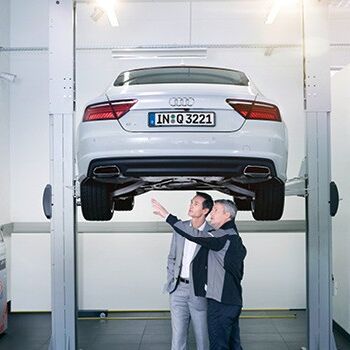 Zwei Männer begutachten ein angehobenes Audi-Fahrzeug.