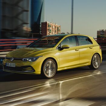 Ein gelber Volkswagen Golf 8 fährt bei Sonnenuntergang auf einer Stadtstraße. | Volkswagen Zentrum Passau