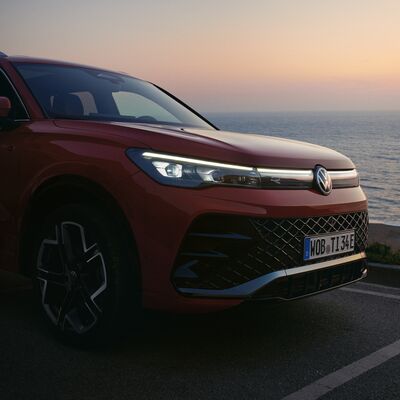 Ein roter Volkswagen steht bei Sonnenuntergang am Meer, präsentiert von Erich Röhr GmbH & Co. KG.