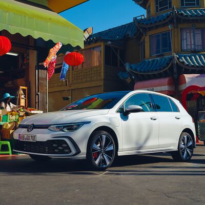 Weißer Volkswagen Golf GTE vor einem asiatischen Markt mit Laternen. | Škoda Auto Röhr.