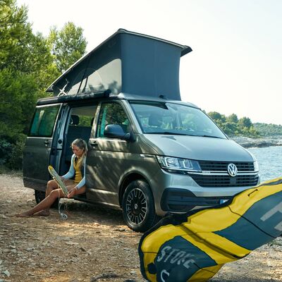 Frau entspannt sich neben einem Volkswagen Camper am Seeufer. | © Auto Röhr