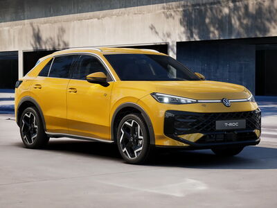 Ein gelber Volkswagen T-Roc R-Line parkt elegant vor einem modernen Gebäude, beworben von Auto Röhr.