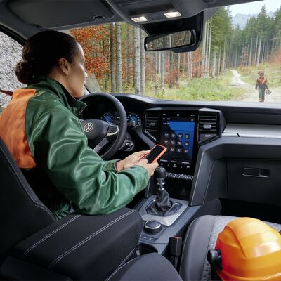 Frau am Steuer eines Volkswagen im Wald, nutzt Smartphone. Škoda Auto Röhr.
