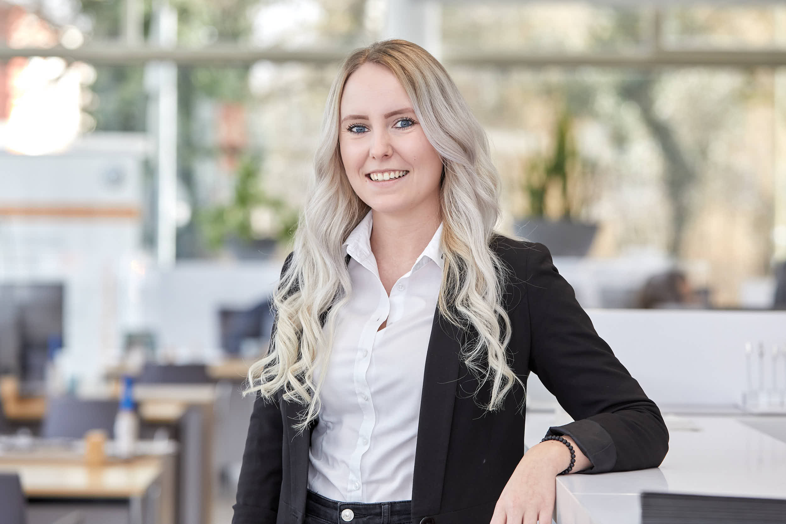 Lächelnde Frau in einem modernen Büro von Auto Röhr, elegant gekleidet in Blazer und Hemd.